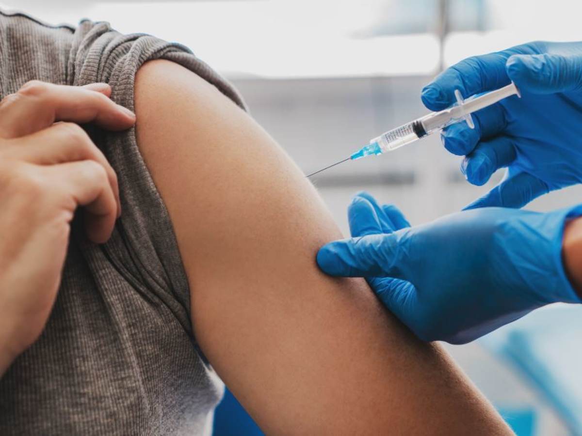 Man receiving a vaccination in left arm by nurse in teal blue surgical gloves